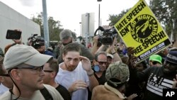 A supporter of white nationalist Richard Spencer, center in white shirt, tries to cover up as he clashes with the crowd after a speech by Spencer, Oct. 19, 2017, at the University of Florida in Gainesville.