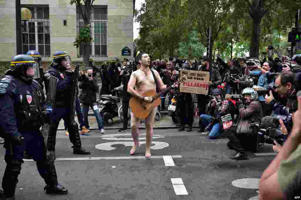 A naked man playing guitar stands in front of police officers during a protest called by several French unions against the law reform in Paris.