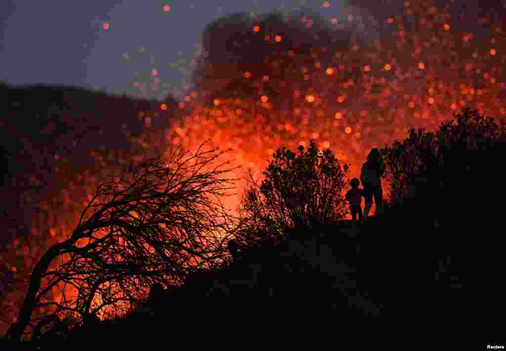 A woman climbs a hill with a child to see the Cumbre Vieja volcano as it continues to erupt in Tacande de Arriba on the Canary Island of La Palma, Spain, Oct 2, 2021.