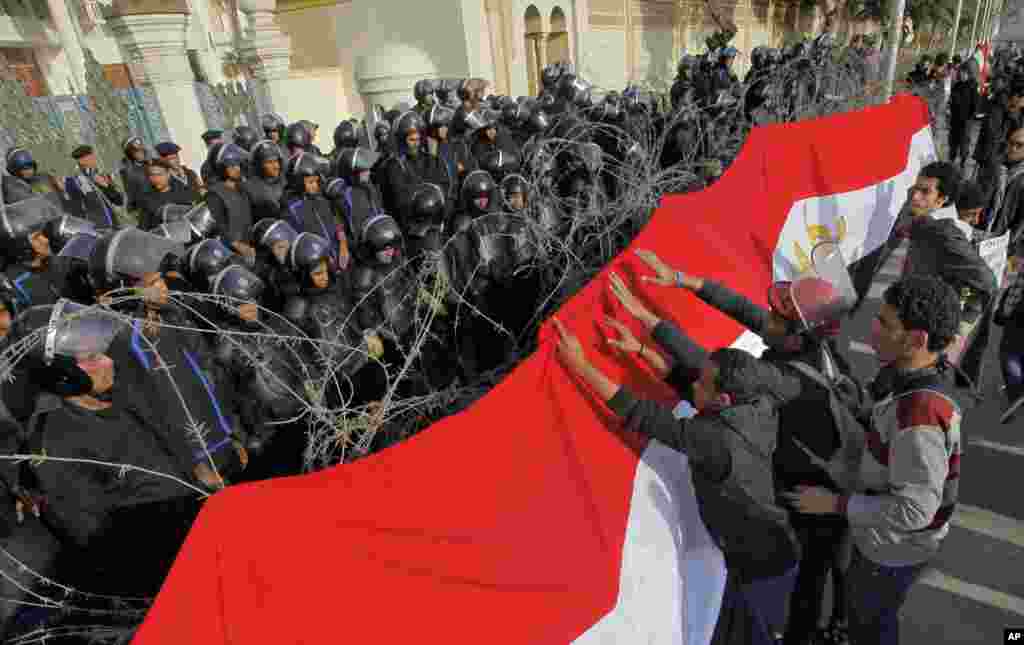 Egyptian protesters hang a giant banner in the colors of Egypt’s national flag on barbed wires in front of anti-riot soldiers at the entrance to the presidential palace in Cairo.