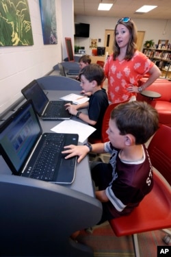 May 8, 2019, photograph, Sharon Stidham, standing, talks to her sons Graham, center, and Miles, front, as they use the laptops at East Webster High School to do homework in Maben, Miss. The internet signal does not reach their house. (AP Photo/Rogelio V. Solis)