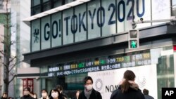 Para pejalan kaki terlihat mengenakan masker saat melewati papan kampanye Olimpiade Tokyo di depan kantor sekuritas di Tokyo, Jepang, 29 Januari 2021. 
