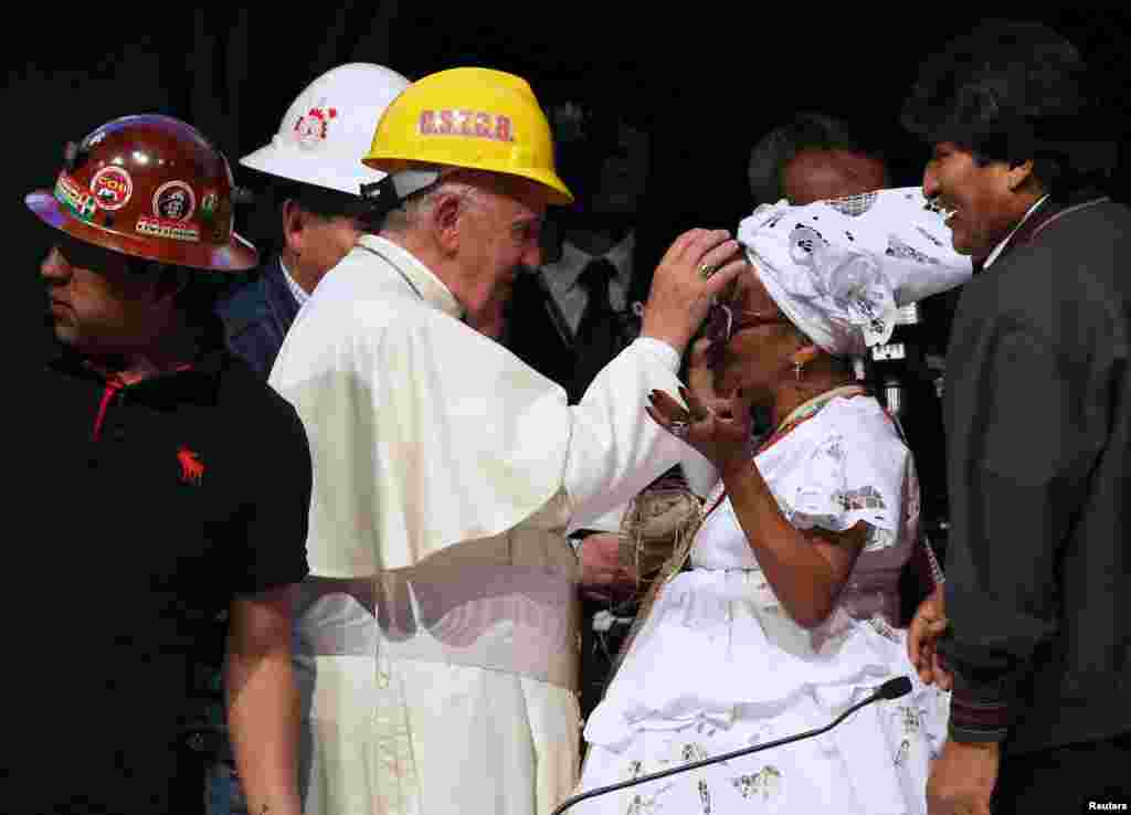 Pope Francis, wearing a helmet, blesses a woman as Bolivian President Evo Morales looks on during a World Meeting of Popular Movements in Santa Cruz, July 9, 2015.