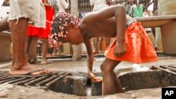 FILE - An Angolan child washes in a ditch near a water pump in Luanda.