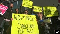 FILE - Protesters hold up signs outside a courthouse where a federal judge hears arguments in a lawsuit challenging President Donald Trump's executive order to withhold funding from communities that limit cooperation with immigration authorities, in San Francisco, California, April 14, 2017.