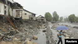 A woman holding an umbrella walks past near damaged houses by recent flooding in Kujang district, in the province of North Pyongan, August 28, 2012. 