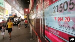 People walk past an electronic board showing the Hong Kong share index outside a local bank in Hong Kong, Monday, Aug. 24, 2015.