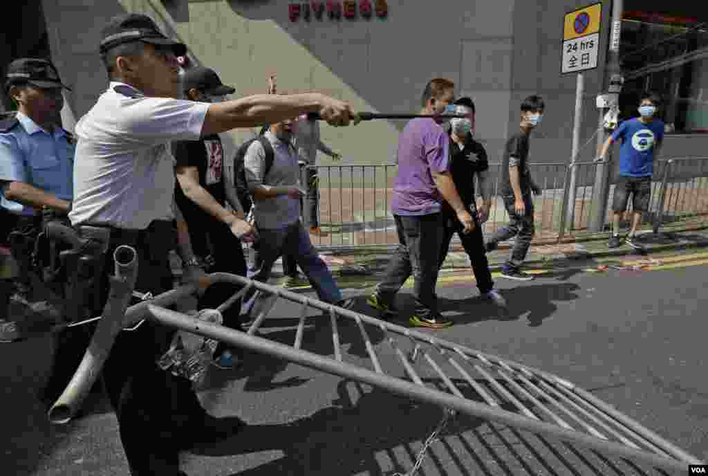 A police officer tries to stop a man who is removing the metal barricades that protesters set up to block off main roads near the heart of the city's financial district, Hong Kong, Oct. 13, 2014.