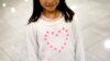 FILE - Janet Mejia, 7, wears a sweater bearing a heart as she waits for two siblings to arrive from El Salvador in Linthicum, Md., Nov. 12, 2015. They were among the first teens to receive permission to travel legally to the U.S. via the Central American Minors program.
