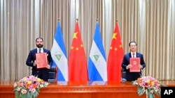 在这张中国官方新华社发布的照片中，尼加拉瓜总统丹尼尔·奥尔特加的儿子兼顾问雷亚诺·奥尔特加-穆里略和中国外交部副部长马朝旭展示他们共同签署的关于恢复外交关系的公报。（资料照片：2021年12月10日）