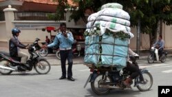 A Cambodian man, right, drive his motorbike overloaded with vegetable sacks as he passes a traffic police officer, center, in Phnom Penh, Cambodia, Tuesday, Aug. 25, 2015. (AP Photo/Heng Sinith)