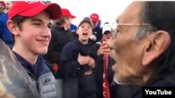 This image, taken from YouTube, shows a youth in a MAGA hat staring at and standing extremely close to Nathan Phillips, a 64-year-old Native American man singing and playing a drum, at the Indigenous Peoples March in Washington, Jan. 18, 2019. 