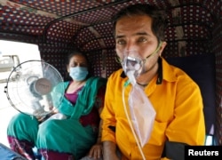 A patient wearing an oxygen mask looks on as his wife holds a battery-operated fan while waiting inside an auto-rickshaw to enter a COVID-19 hospital for treatment, amidst the spread of the coronavirus disease (COVID-19) in Ahmedabad, India, April 25, 202