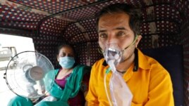 A patient wearing an oxygen mask looks on as his wife holds a battery-operated fan while waiting inside an auto-rickshaw to enter a COVID-19 hospital for treatment, amidst the spread of the coronavirus disease (COVID-19) in Ahmedabad, India, April 25, 2021. (Reuters)