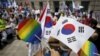 An activist holds up a rainbow-colored fan and a South Korean national flag as gay pride festival participants face Christians opposed to homosexuality in central Seoul, South Korea, June 28, 2015.