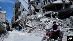 FILE - A man rides past destruction in the town of Douma, the site of a suspected chemical weapons attack, near Damascus, Syria, April 16, 2018. 