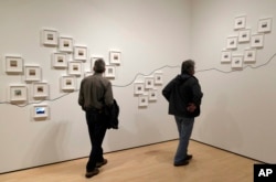 In this March 15, 2018, photo, two men look at the conceptual project "The People's View" by Dutch artist Rein Jelle Terpstra that is part of the exhibit, "The Train: RFK's Last Journey," at the San Francisco Museum of Modern Art in San Francisco. The photographs, taken by bystanders, are arranged on the wall by where they were taken on the route from New York City to Washington.