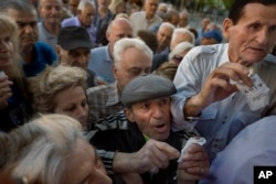 Пензионери со редни броеви во раката пред влезот на банка во Атина