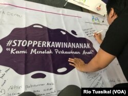 Seorang laki-laki membubuhkan pesan menolak perkawinan anak di atas spanduk yang dipajang dalam Festival Kabupaten/Kota Layak Anak (KLA) yang digelar di Bandung, Minggu (16/12/2018) siang. (Foto: Rio Tuasikal/VOA)