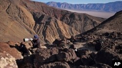 FILE - Jason O. Watson looks through a telephoto lens on a cliff overlooking the nicknamed Star Wars Canyon in Death Valley National Park, Calif., Feb. 28, 2017.