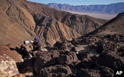 FILE - Jason O. Watson looks through a telephoto lens on a cliff overlooking the nicknamed Star Wars Canyon in Death Valley National Park, California, Feb. 28, 2017.