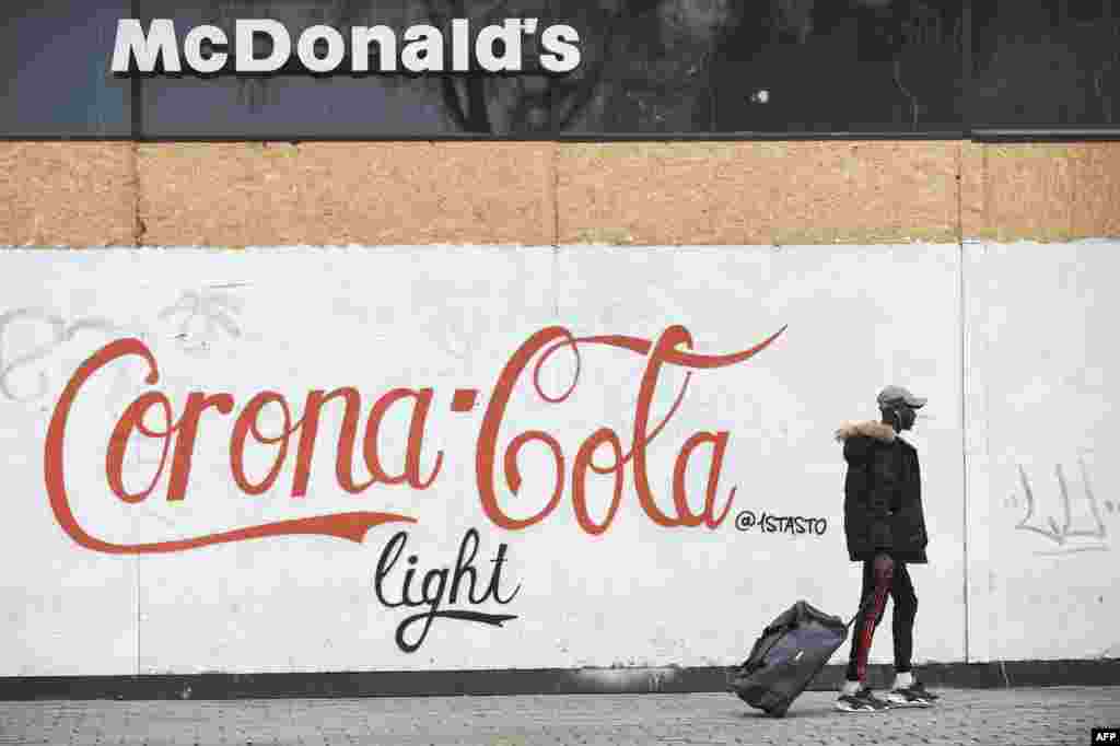 A man walks past a graffiti on a wall of a closed McDonald&#39;s fast restaurant, reading &quot;Corona Cola light&quot;, in Nantes, western France, March 17, 2020 while a strict lockdown comes into effect to stop the spread of the COVID-19 in the country.