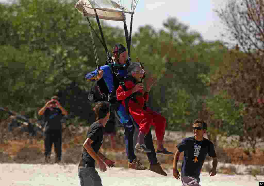 Centenarian Georgina Harwood, center right, gestures as she lands with Jason Baker, centre left, after her tandem parachute jump forming part of her birthday celebrations, in Cape Town, South Africa, March 14, 2015. Harwood, who celebrated her 100th birthday, completed her third parachute jump in front of family and friends.