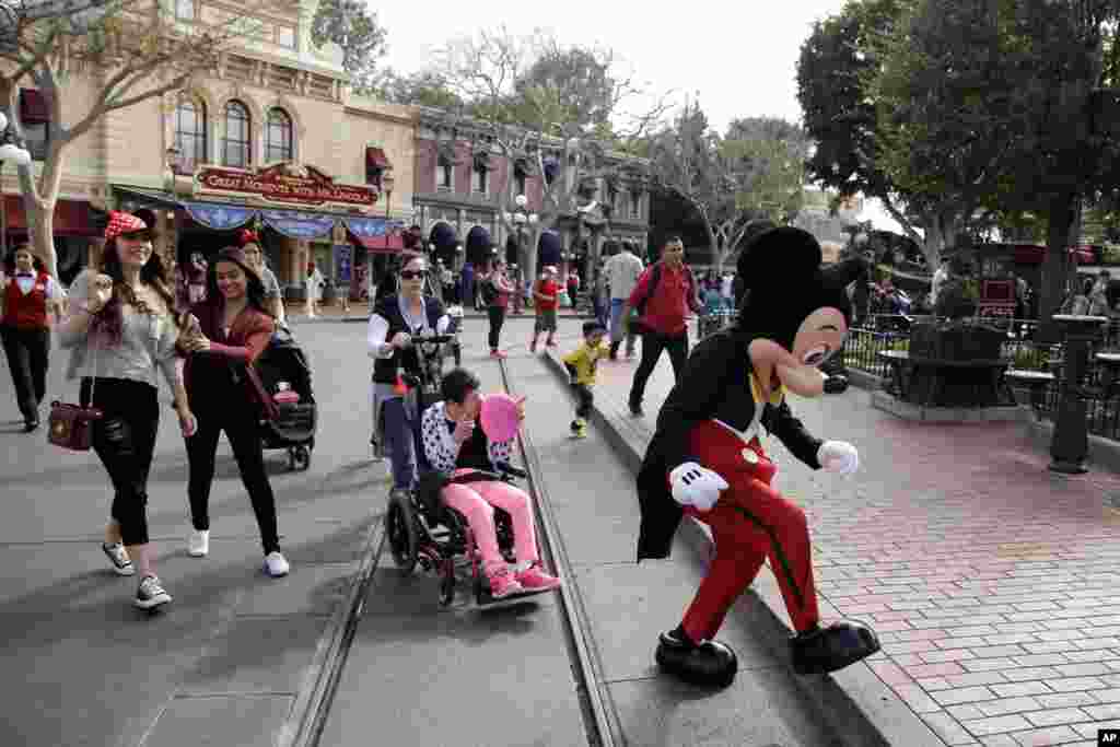 In this Jan. 22, 2015, file photo, visitors follow Mickey Mouse for photos at Disneyland in Anaheim, Calif. Disneyland, the original theme park, opened in 1955. Company founder Walt Disney oversaw its construction on a 65-hectare (160-acre) orange farm in