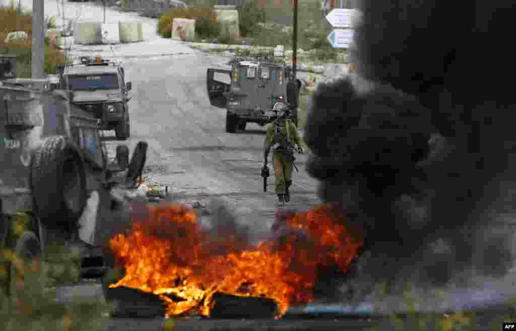 A member of the Israeli security forces walks behind burning tires during clashes with Palestinian protesters at the entrance of the Palestinian town of Al-Bireh on the outskirts of Ramallah in the Israeli-occupied West Bank.