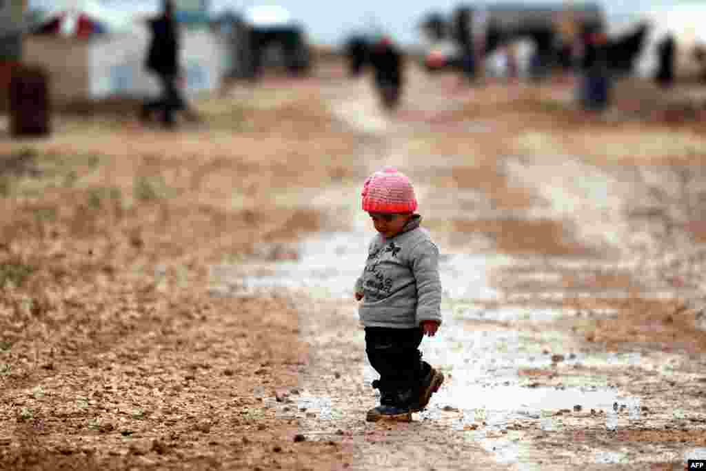 A young boy who was displaced with families from Deir al-Zor and its surroundings, walks in the mud at a camp for displaced people near the town of al-Arishah in the northeastern Syrian Hasaka province.
