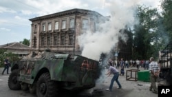 Cư dân địa phương vây quanh một chiếc xe quân sự bị đốt cháy tại hiện trường một vụ giao tranh giữa quân đội Ukraine và những chiến binh thân Nga ở Mariupol, 13/6/2014.