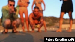 Beachgoers observe a tiny sea turtle that just hatched trying to reach the Mediterranean’s warm waters on Cyprus’ Lara Beach.