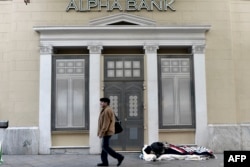 A man walks past a bank next a homeless sleeping on the pavement in central Athens, Greece, Feb. 28, 2017.