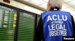 FILE - An American Civil Liberties Union legal observer watches a flight arrivals board, as dozens of pro-immigration demonstrators greeted international passengers arriving at Dulles International Airport, Jan. 29, 2017.