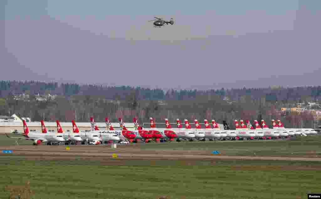 The Swiss Army Eurocopter EC635 flies over the aircrafts of the Swiss Airlines, the Edelweis Air and the Helvetic Airways parked at an airbase in Duebendorf, Switzerland.
