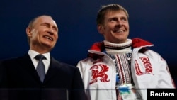FILE: Russian President Vladimir Putin, left, laughs with Russia's gold medalist bobsleigh athlete, Alexander Zubkov, during the 2014 Sochi Winter Olympics closing ceremony Feb. 23, 2014.