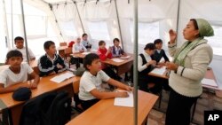 FILE - Children listen to their teacher during a lesson at a local school, based in a tent, in the city of Osh, Kyrgyzstan.