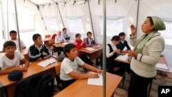 FILE - Children listen to their teacher during a lesson at a local school, based in a tent, in the city of Osh, Kyrgyzstan.