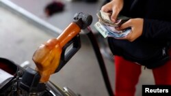 FILE - A worker at a state-owned Pertamina petrol station holds money as a motorcycle is filled with subsidised fuel in Jakarta, Oct. 31, 2014. 