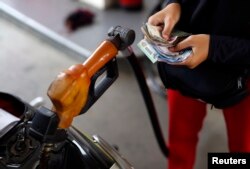 Seorang pekerja di SPBU Pertamina memegang uang saat sepeda motormengisi BBM bersubsidi di Jakarta, 31 Oktober 2014. (Foto: Reuters)