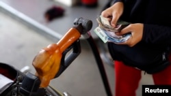 FILE - A worker at a state-owned Pertamina petrol station holds money as a motorcycle is filled with subsidized fuel in Jakarta, Oct. 31, 2014. 