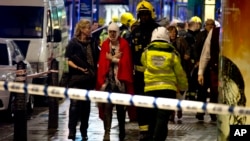 A woman stands bandaged and wearing a blanket given by emergency services following an incident at the Apollo Theatre, in London's Shaftesbury Avenue, Thursday evening, Dec. 19, 2013, during a performance at the height of the Christmas season.