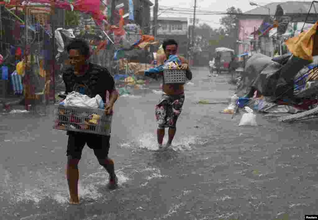 Warga membawa barang-barang mereka saat Topan Rammasun menghantam kota Imus, Cavite, di barat daya Manila (16/7). (Reuters/Erik De Castro)