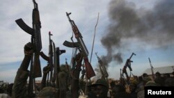 Rebel fighters hold up their rifles as they walk in front of a bushfire in rebel-controlled territory in Upper Nile State, South Sudan, Feb. 13, 2014. 