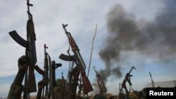 Rebel fighters hold up their rifles as they walk in front of a bushfire in a rebel controlled territory in Upper Nile State, South Sudan, Feb. 13, 2014. 