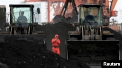 FILE - An employee walks between front-end loaders which are used to move coal imported from North Korea at Dandong port in the Chinese border city of Dandong, Liaoning province, Dec. 7, 2010. 