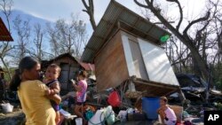 ພວກຊາວບ້ານພາກັນຢືນເບິ່ງ​ຄວາມ​ເສຍ​ຫາຍ ຫຼັງຈາກລົມ​ໄຕ້​ຝຸ່ນໄຣ (Rai) ພັດ​ເຂົ້າ​ຖະ​ຫຼົ່ມ ຢູ່ເມືອງຕາລິໄຊ (Talisay) ປະເທດຟິລິບປິນ ວັນທີ 18 ທັນວາ 2021. 