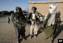 FILE - Taliban militants stand beside the burnt trucks, background left, on main Ghazni- Kandahar highway in Ghazni, west of Kabul, Afghanistan, Oct.19, 2009.