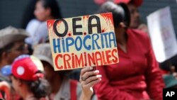 A supporter of Venezuela's president Nicolas Maduro, holds a sign that reads in Spanish "OAS Hypocrites, Criminals" during a government rally in Caracas, Venezuela,, April 27, 2019. 