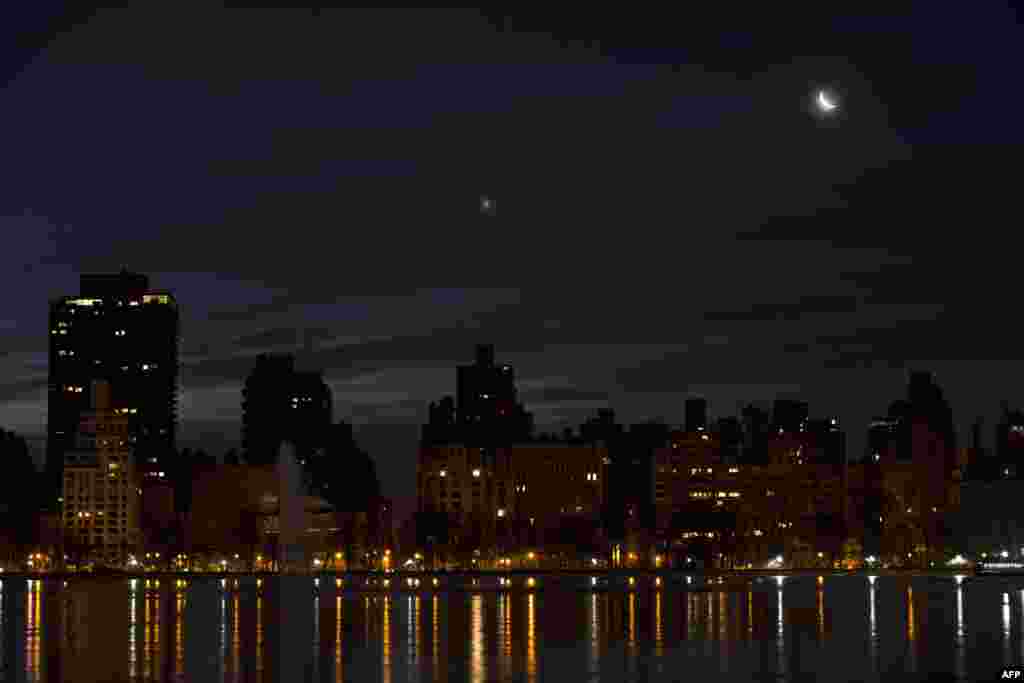 A crescent moon and Venus (L) rise in the pre-dawn hours over the east side of Manhattan in New York.